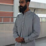 Man wearing a white premium textured striped shirt with sunglasses, standing outdoors near greenery and a sidewalk, styled for a modern yet traditional look.