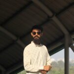 Man wearing a white premium textured striped shirt with sunglasses, standing outdoors near greenery and a sidewalk, styled for a modern yet traditional look.