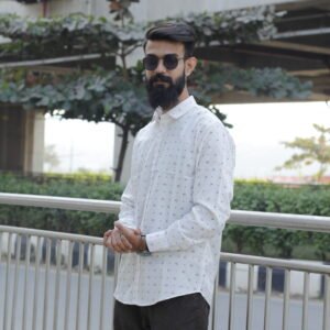 Man wearing a white premium textured striped shirt with sunglasses, standing outdoors near greenery and a sidewalk, styled for a modern yet traditional look.