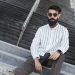 Man wearing a white premium textured striped shirt with sunglasses, standing outdoors near greenery and a sidewalk, styled for a modern yet traditional look.